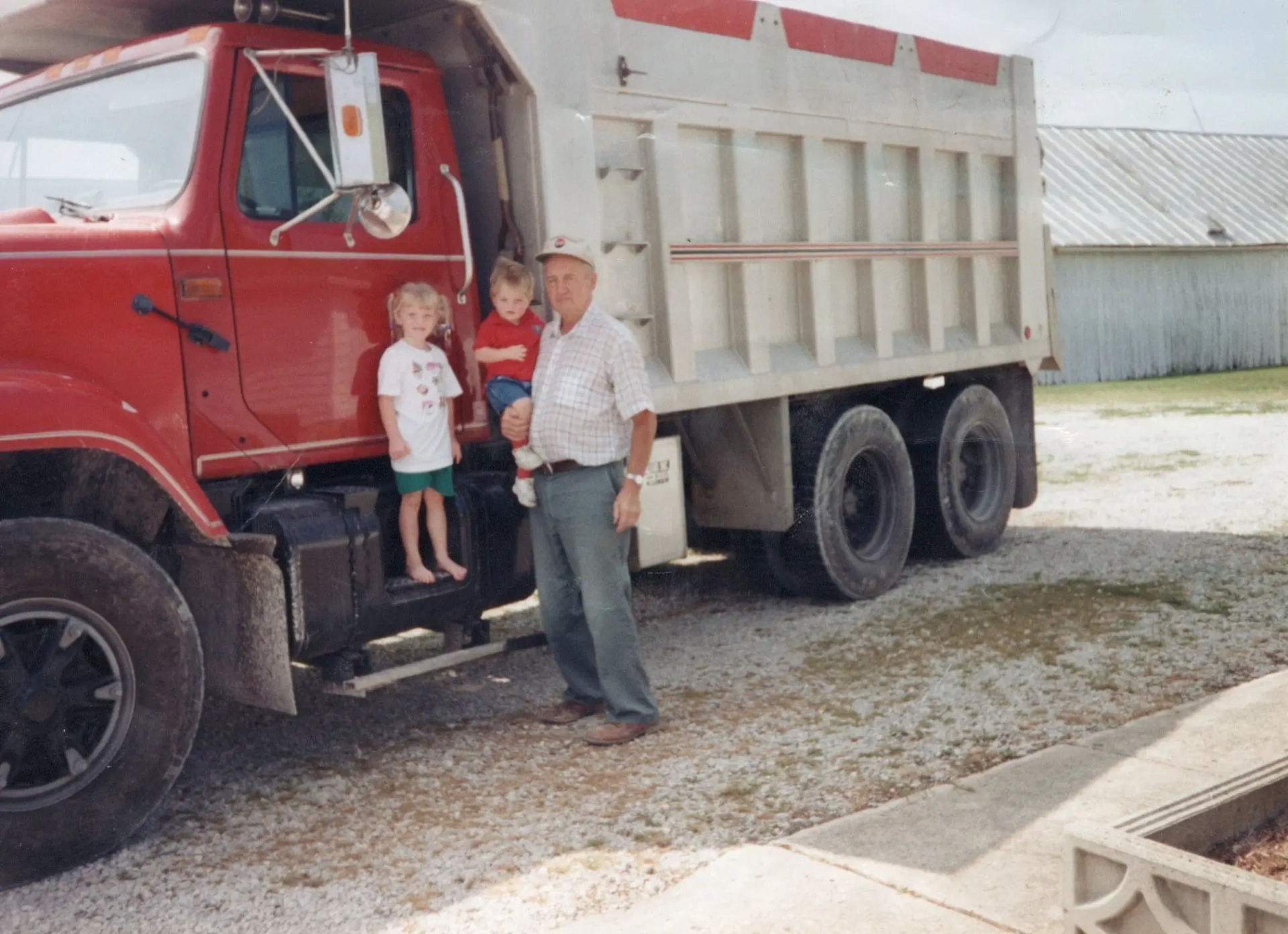 Craig and his grandpa by a large red dump truck.
